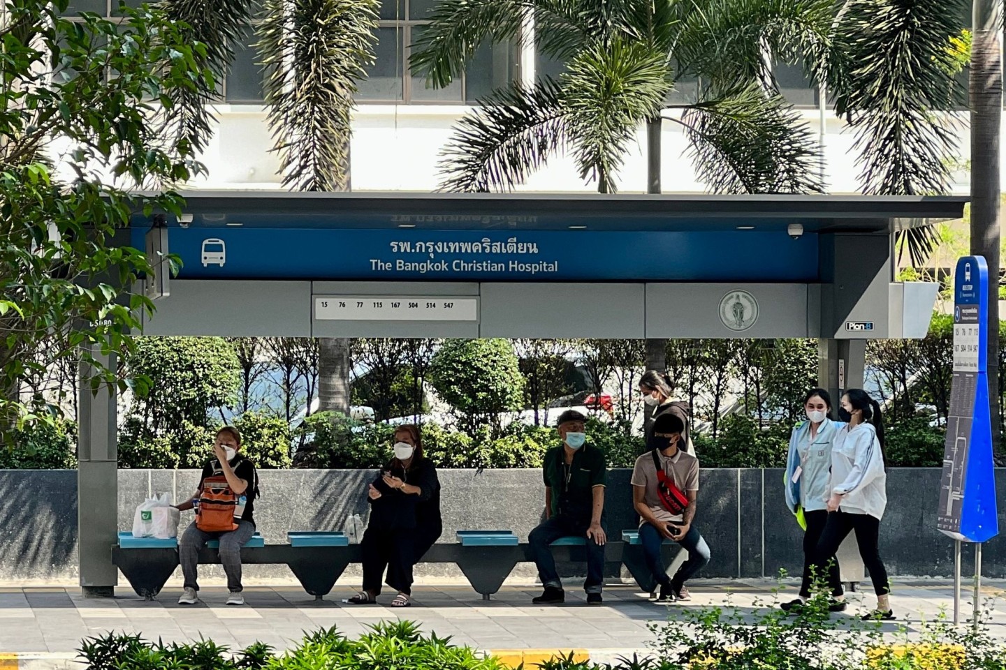 Menschen suchen im Schatten einer Bushaltestelle in Bangkok Schutz vor der Sonne.