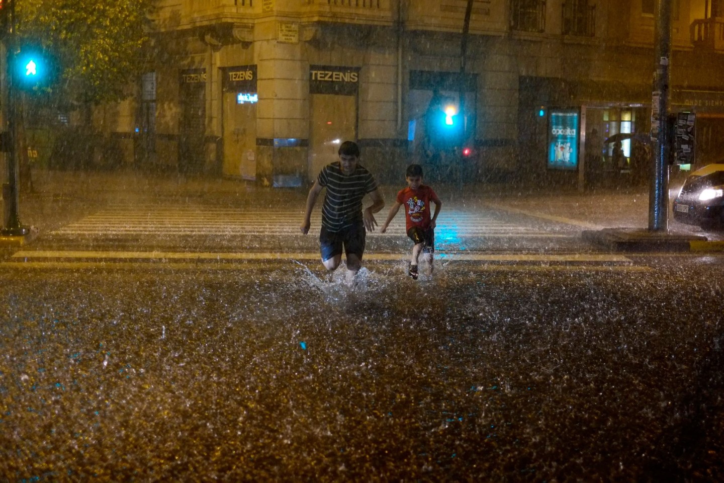 Menschen überqueren bei starkem Regen eine überschwemmte Straße in Pamplona.