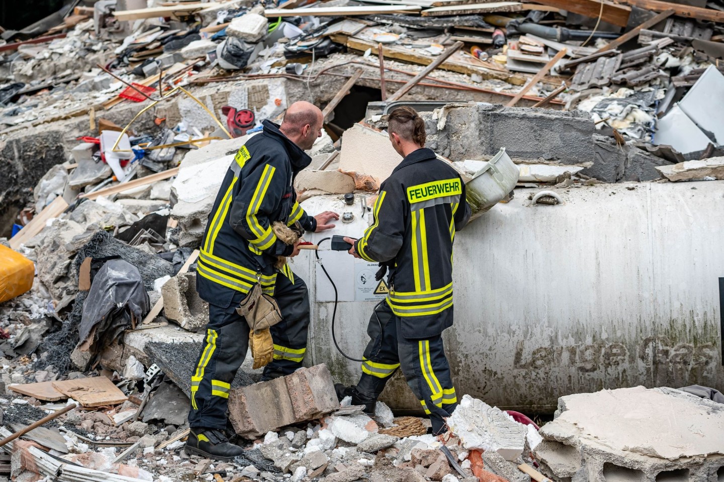 Feuerwehrleute machen zwischen den Trümmern eine Messung an einem Gastank.
